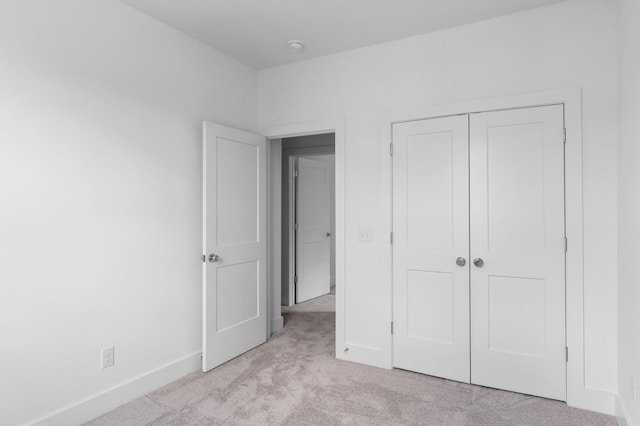 unfurnished bedroom featuring a closet, light colored carpet, and baseboards