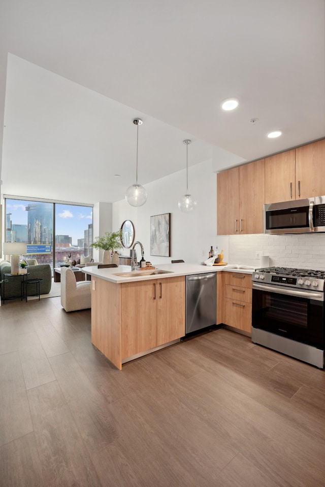 kitchen with light brown cabinets, a sink, open floor plan, a peninsula, and appliances with stainless steel finishes