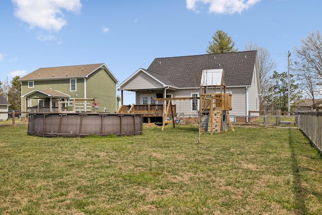back of property with a wooden deck, a lawn, a fenced backyard, and a fenced in pool