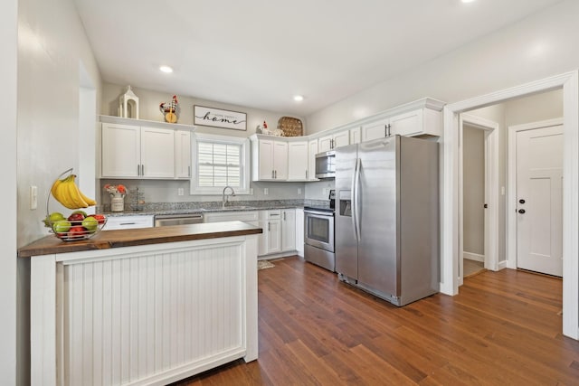 kitchen featuring stainless steel appliances, a peninsula, dark wood-style flooring, white cabinetry, and wooden counters