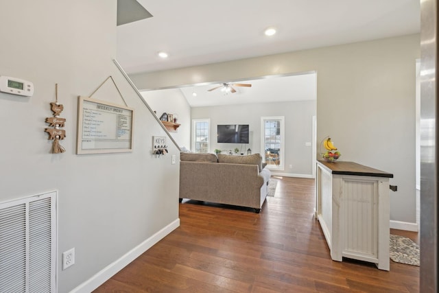 living room featuring dark wood-type flooring, visible vents, baseboards, and a ceiling fan