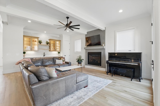 living area featuring baseboards, light wood finished floors, beam ceiling, and crown molding