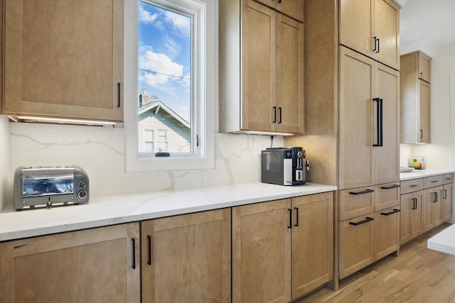 kitchen featuring light wood-type flooring, backsplash, light brown cabinetry, and light stone countertops