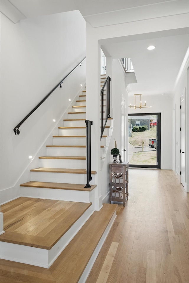 stairs with an inviting chandelier, baseboards, a wealth of natural light, and wood finished floors