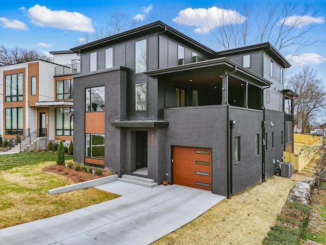 contemporary home featuring an attached garage, central AC, brick siding, a sunroom, and driveway