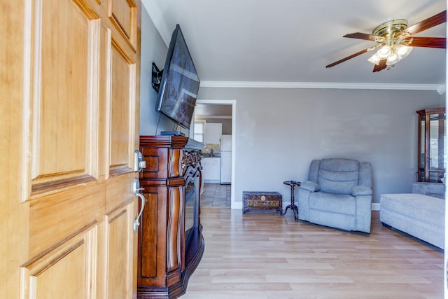 living area with light wood-style floors, baseboards, ornamental molding, and a ceiling fan