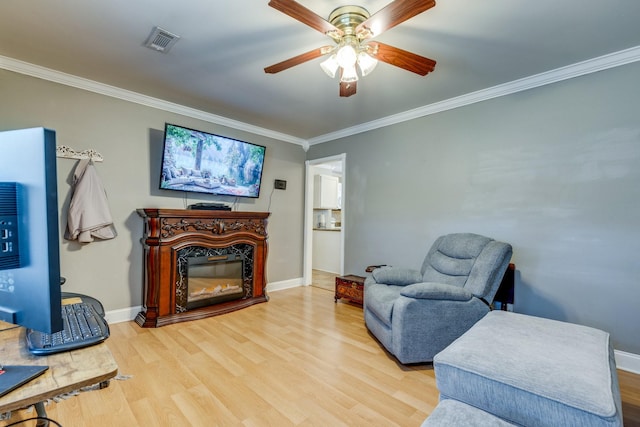 living area featuring crown molding, visible vents, wood finished floors, and a glass covered fireplace