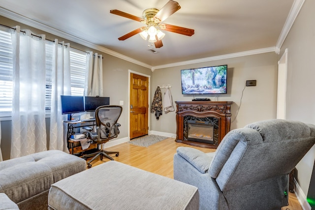 office featuring visible vents, baseboards, a glass covered fireplace, crown molding, and light wood-style floors