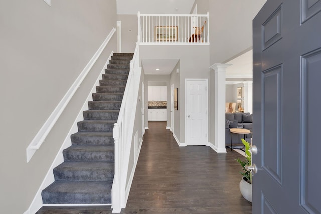 foyer entrance with dark wood-style flooring, ornate columns, a towering ceiling, baseboards, and stairs