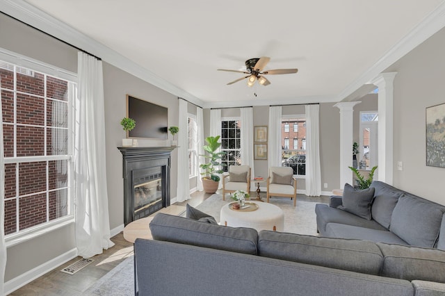 living room with ornamental molding, a glass covered fireplace, visible vents, and ornate columns