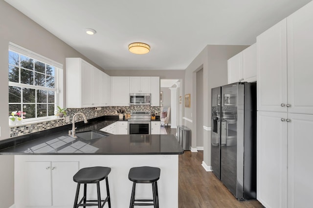 kitchen featuring stainless steel appliances, dark countertops, white cabinetry, a sink, and a peninsula