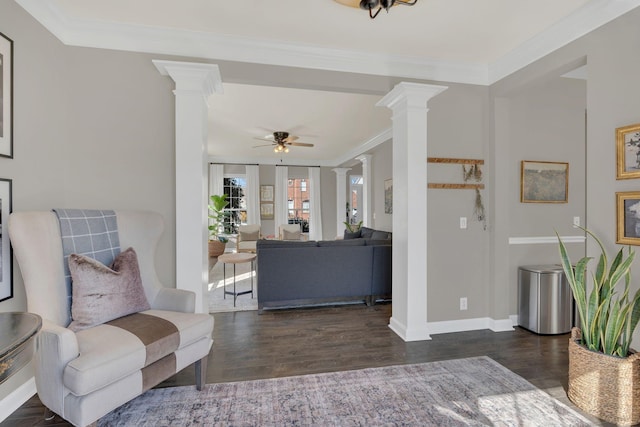 living area featuring baseboards, ceiling fan, wood finished floors, crown molding, and ornate columns