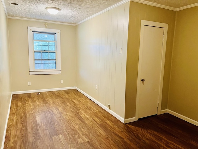 empty room featuring baseboards, visible vents, wood finished floors, a textured ceiling, and crown molding