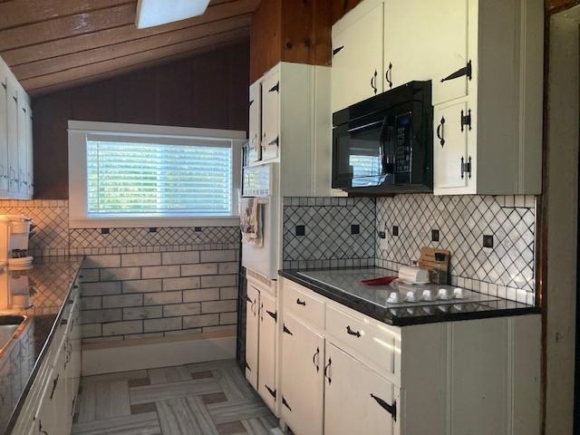 kitchen with black microwave, vaulted ceiling, and white cabinetry