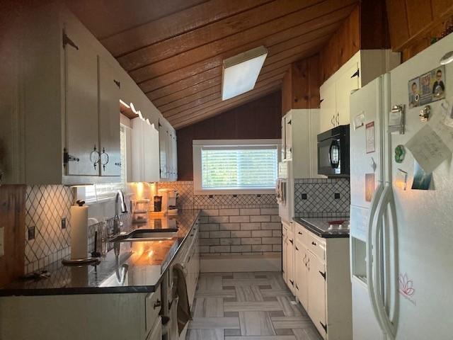 kitchen featuring tasteful backsplash, dark countertops, vaulted ceiling, black appliances, and a sink