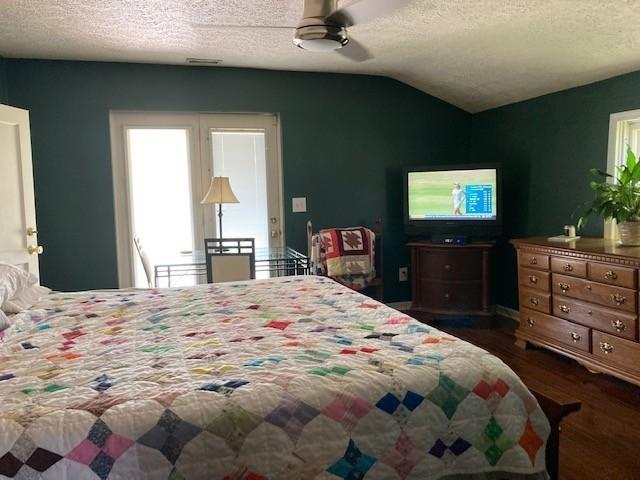 bedroom featuring visible vents, dark wood finished floors, a ceiling fan, vaulted ceiling, and a textured ceiling