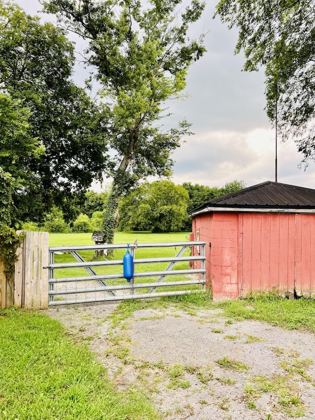 view of gate with a lawn, an outdoor structure, and fence