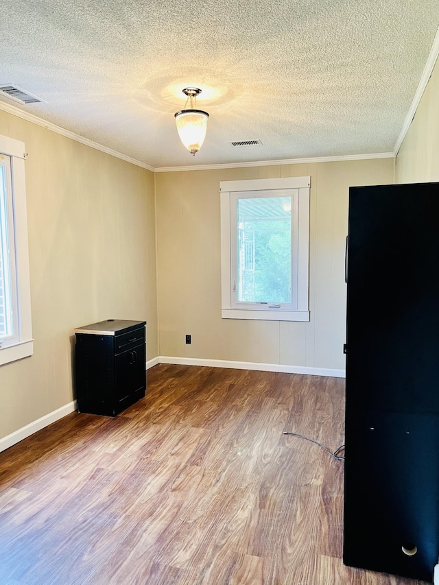 spare room with light wood-type flooring, a textured ceiling, visible vents, and crown molding