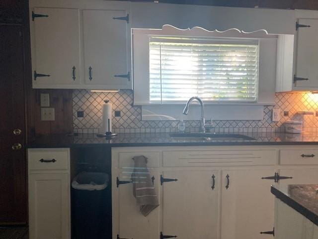 kitchen with tasteful backsplash, dark countertops, a sink, and white cabinets