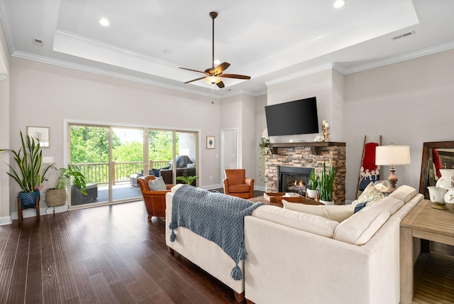 living room featuring a fireplace, visible vents, a raised ceiling, and dark wood-type flooring