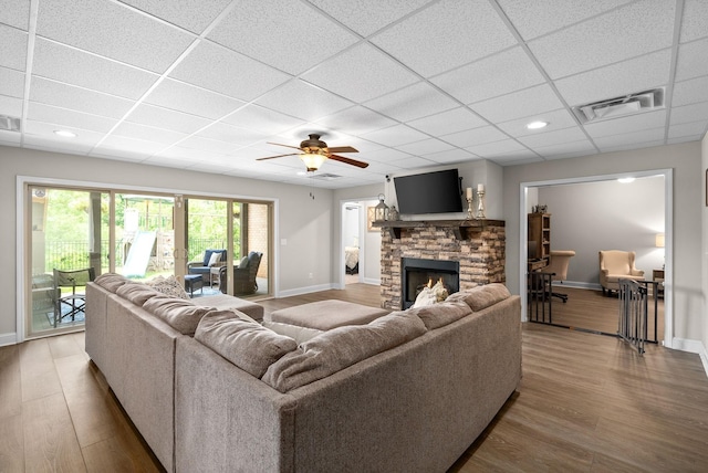 living area with visible vents, a stone fireplace, a drop ceiling, and wood finished floors