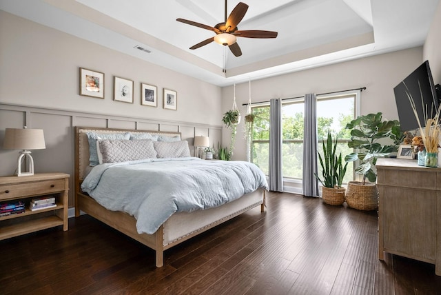 bedroom featuring visible vents, a raised ceiling, a wainscoted wall, wood finished floors, and a decorative wall