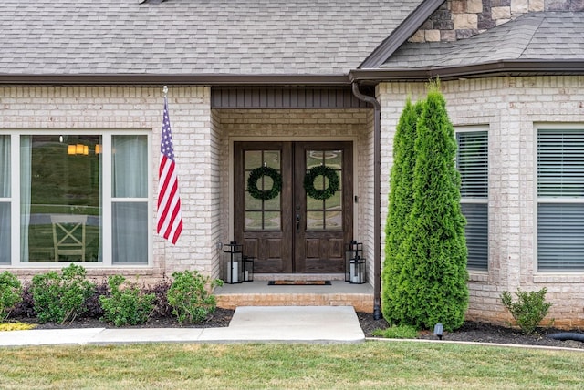 entrance to property with french doors, roof with shingles, and brick siding