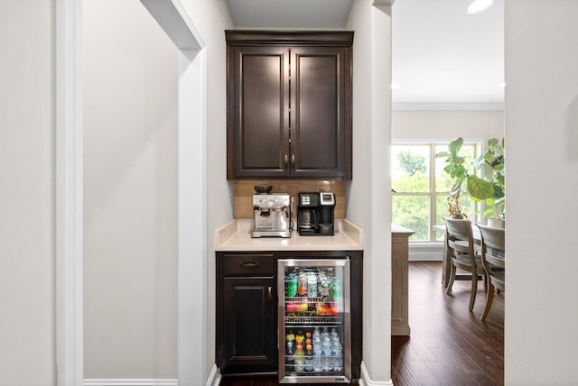 bar featuring beverage cooler, baseboards, dark wood finished floors, crown molding, and a bar