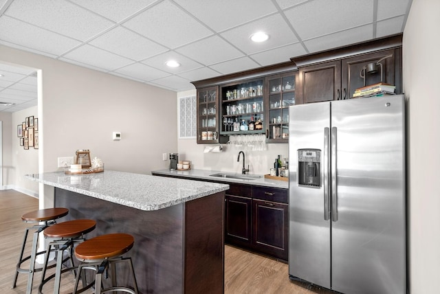 bar featuring a drop ceiling, light wood-style flooring, a sink, stainless steel refrigerator with ice dispenser, and indoor wet bar