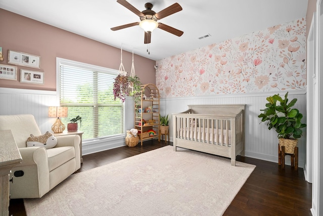 bedroom with a crib, wainscoting, wood finished floors, and wallpapered walls