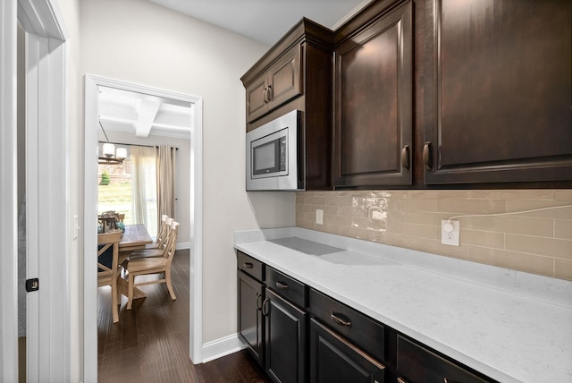 kitchen featuring tasteful backsplash, coffered ceiling, dark wood finished floors, stainless steel microwave, and light countertops