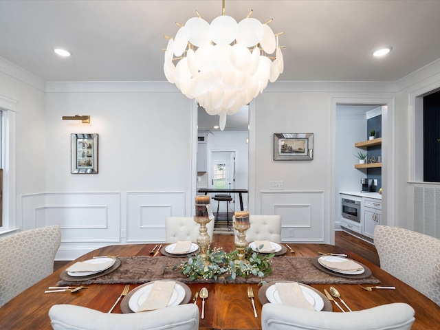 dining area featuring an inviting chandelier, ornamental molding, a decorative wall, and dark wood-type flooring