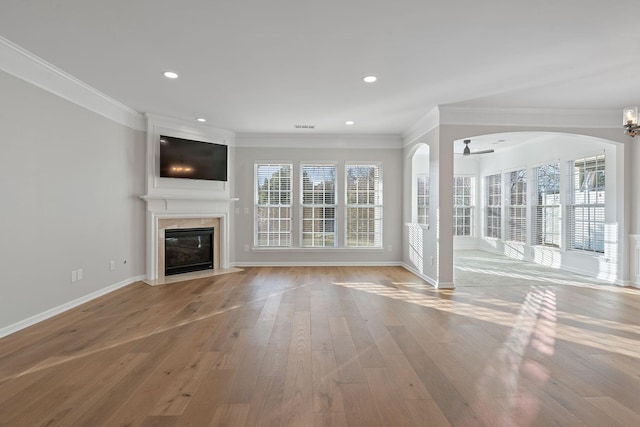 unfurnished living room featuring a fireplace with flush hearth, a ceiling fan, light wood-type flooring, plenty of natural light, and crown molding