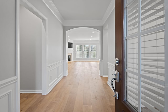 hall with arched walkways, a decorative wall, a wainscoted wall, light wood finished floors, and crown molding