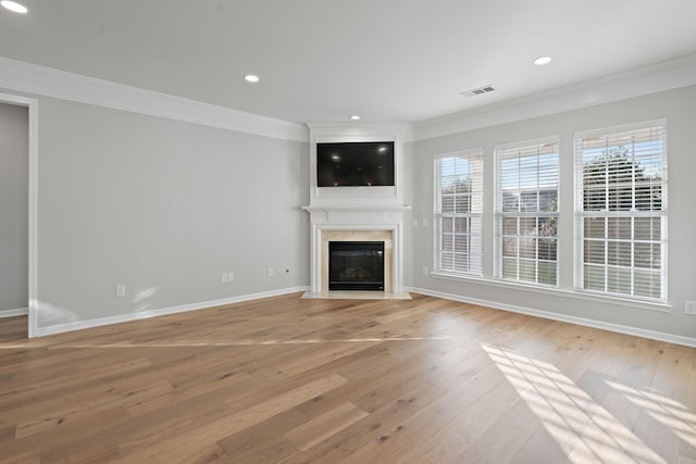 unfurnished living room featuring light wood-style flooring, a fireplace, visible vents, baseboards, and ornamental molding