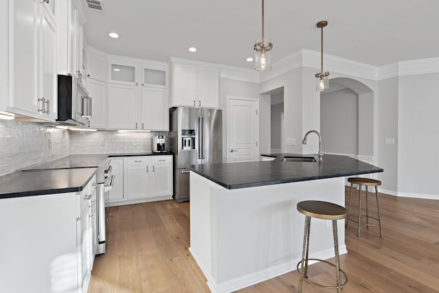 kitchen featuring visible vents, arched walkways, dark countertops, stainless steel appliances, and light wood-style floors