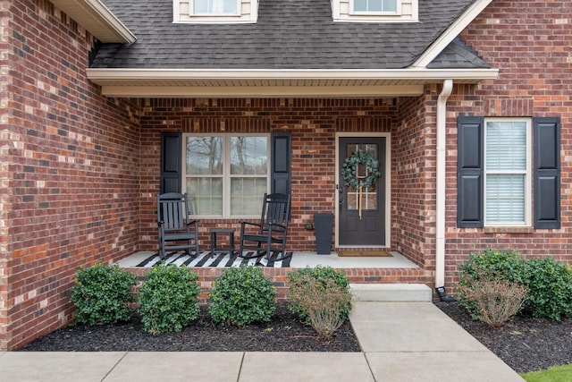 property entrance with a shingled roof, brick siding, and a porch