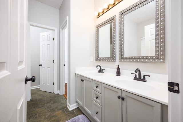 full bath with double vanity, baseboards, and a sink