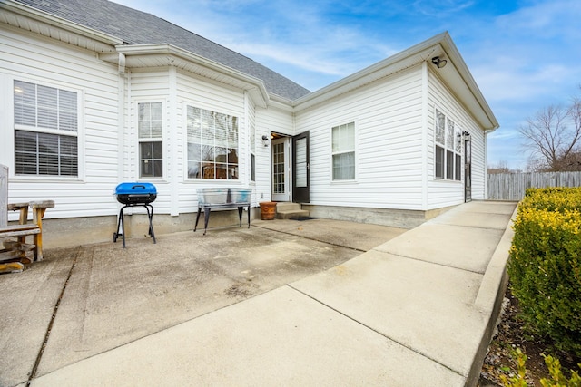 rear view of house featuring a shingled roof, fence, and a patio