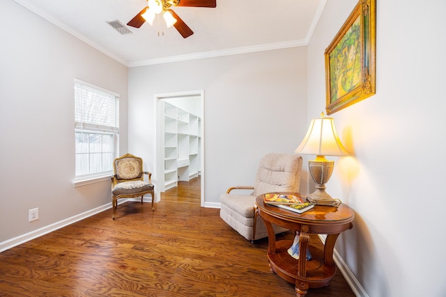 living area with wood finished floors, a ceiling fan, visible vents, baseboards, and ornamental molding