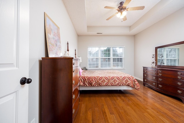 unfurnished bedroom with wood finished floors, a raised ceiling, visible vents, and a ceiling fan