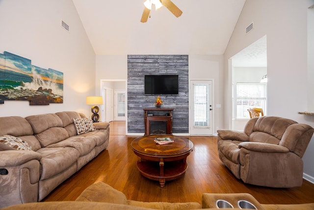 living room featuring high vaulted ceiling, a glass covered fireplace, visible vents, and wood finished floors