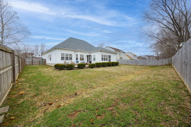 back of property with a fenced backyard, a lawn, and roof with shingles