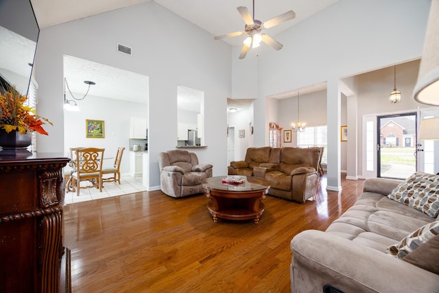 living area featuring baseboards, visible vents, wood finished floors, high vaulted ceiling, and ceiling fan with notable chandelier