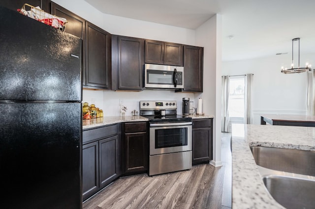 kitchen with dark brown cabinetry, light wood finished floors, appliances with stainless steel finishes, and light stone counters