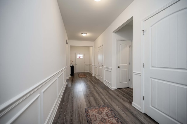 corridor with a wainscoted wall, a decorative wall, and dark wood-style flooring