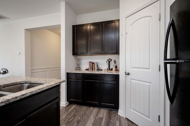 kitchen with dark wood finished floors, freestanding refrigerator, a sink, dark brown cabinets, and light stone countertops