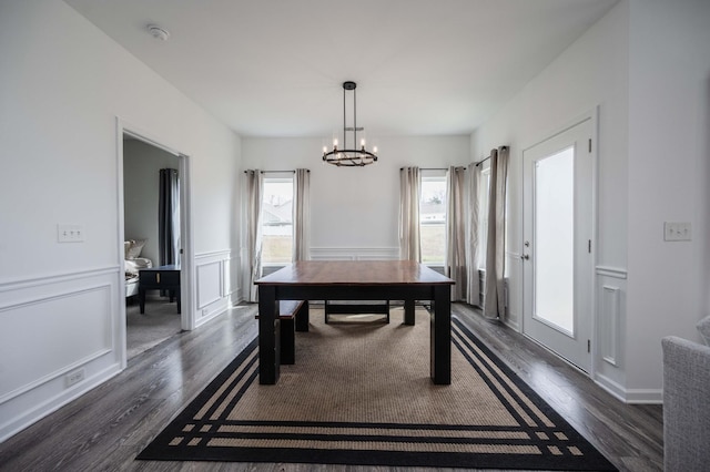 dining space with dark wood-style flooring, a wainscoted wall, a notable chandelier, and a decorative wall