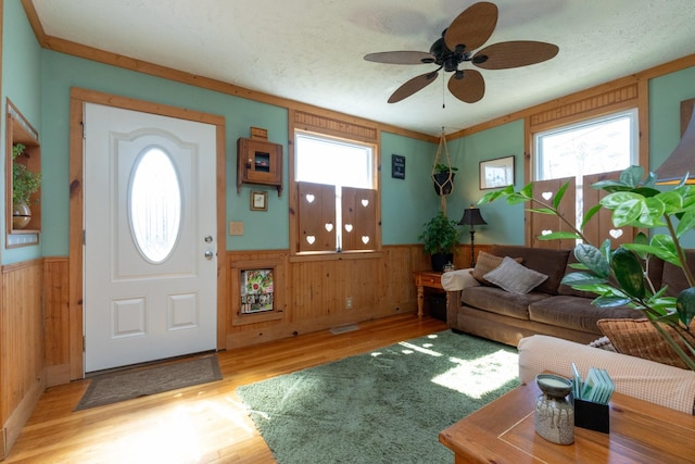 entrance foyer with light wood-style flooring, wainscoting, wood walls, a textured ceiling, and ceiling fan