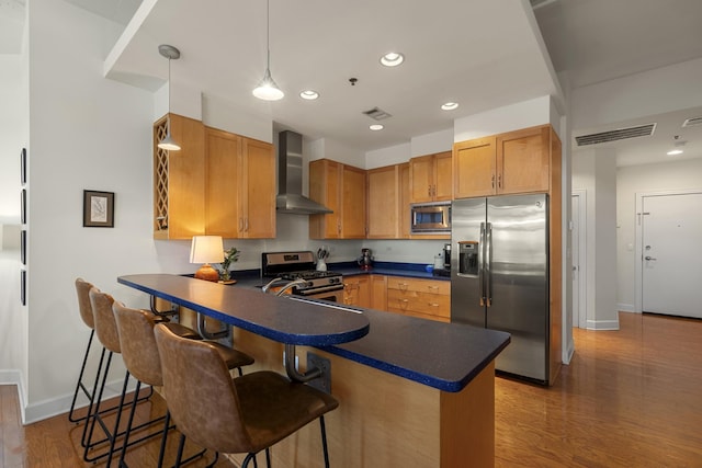 kitchen featuring a peninsula, visible vents, appliances with stainless steel finishes, wall chimney exhaust hood, and dark countertops